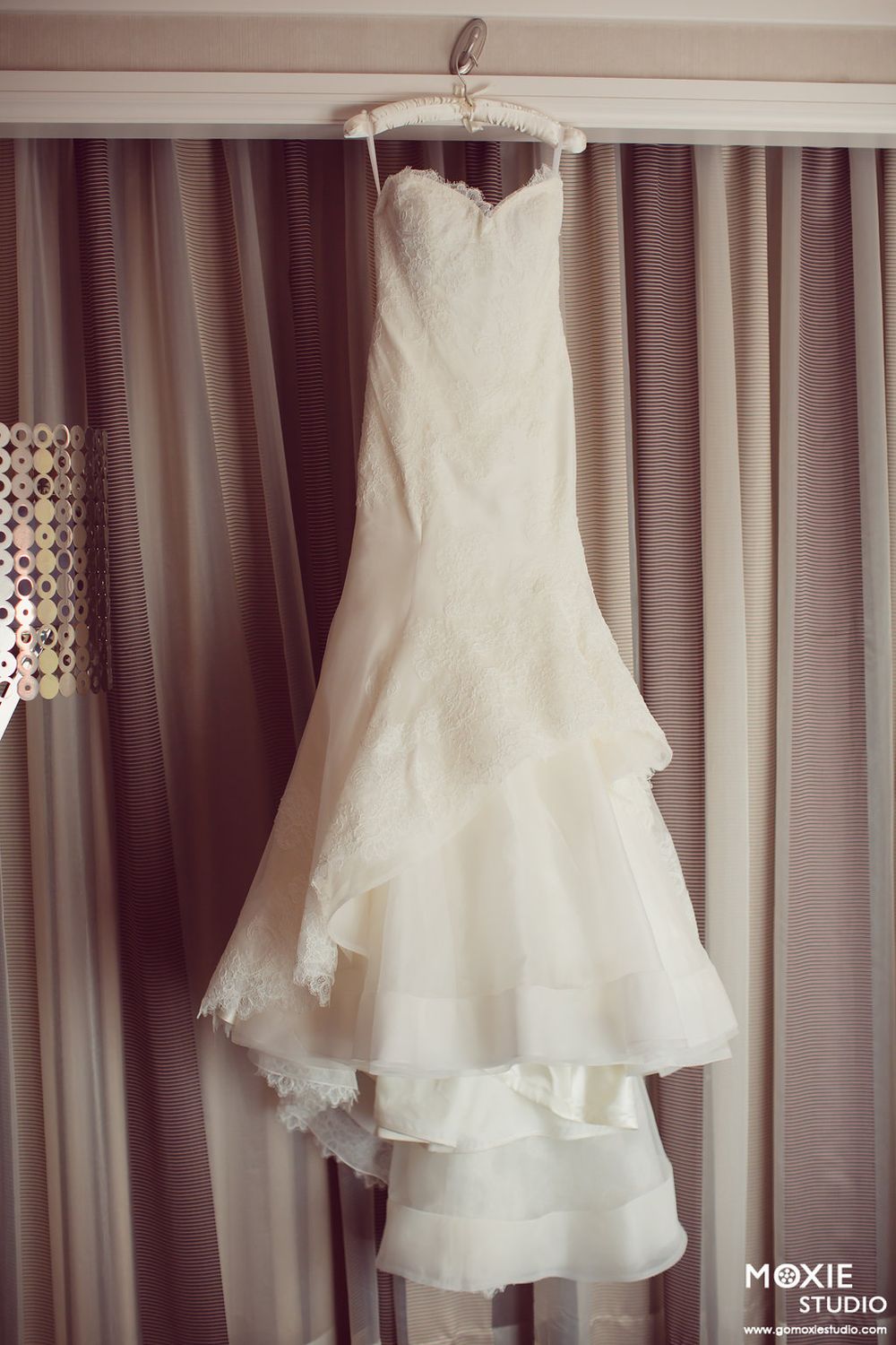 White wedding dress hanging on display against soft curtained background.