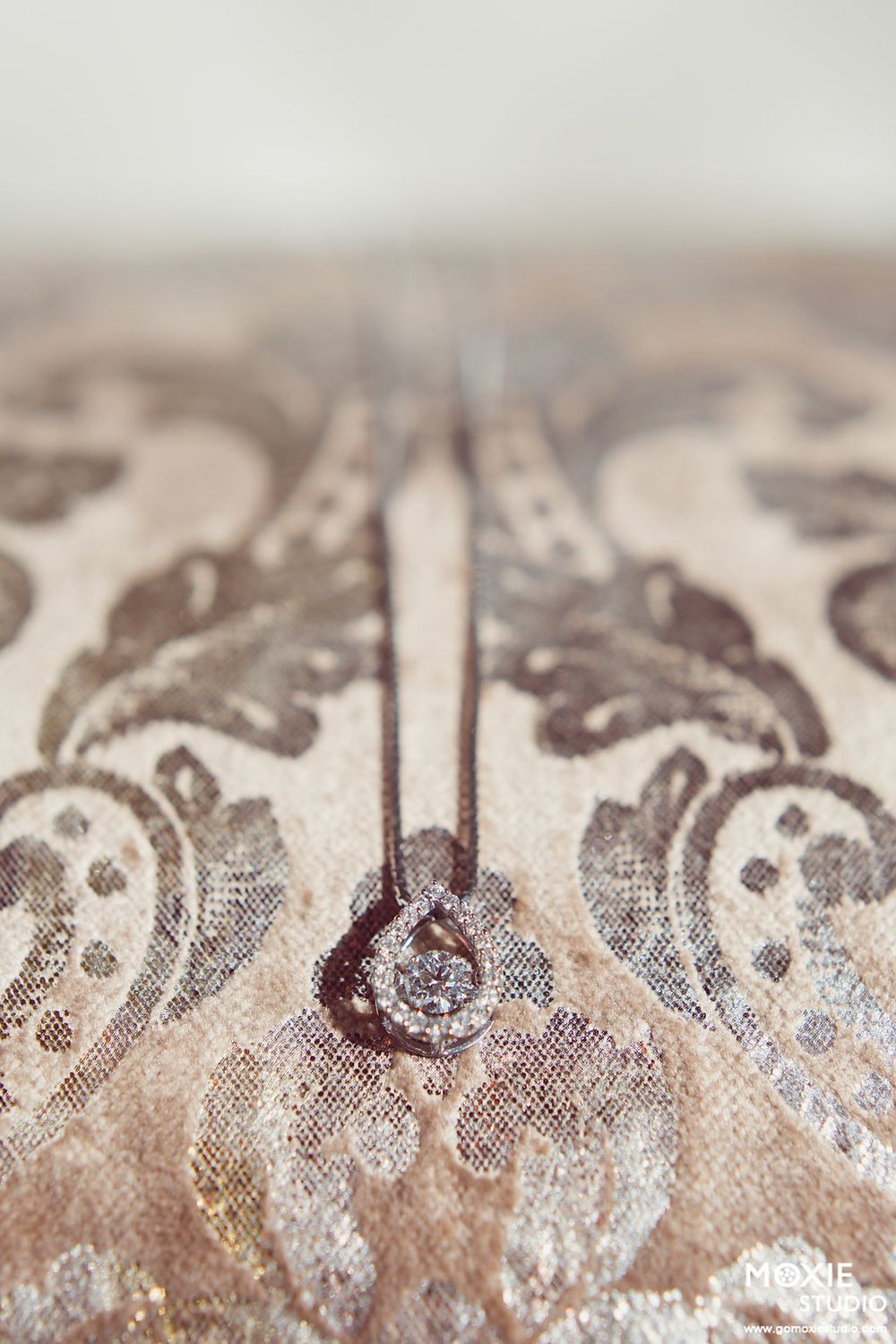 Macro shot of an engagement ring on ornate beige and silver damask fabric pattern.