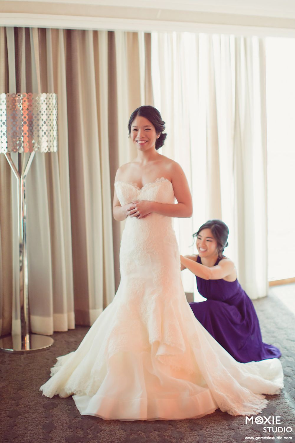 A wedding dress being adjusted and styled in an elegant indoor setting with purple accents.