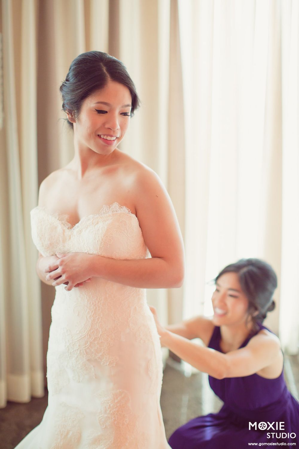 Someone in a white wedding dress being helped with final adjustments by an attendant in purple.