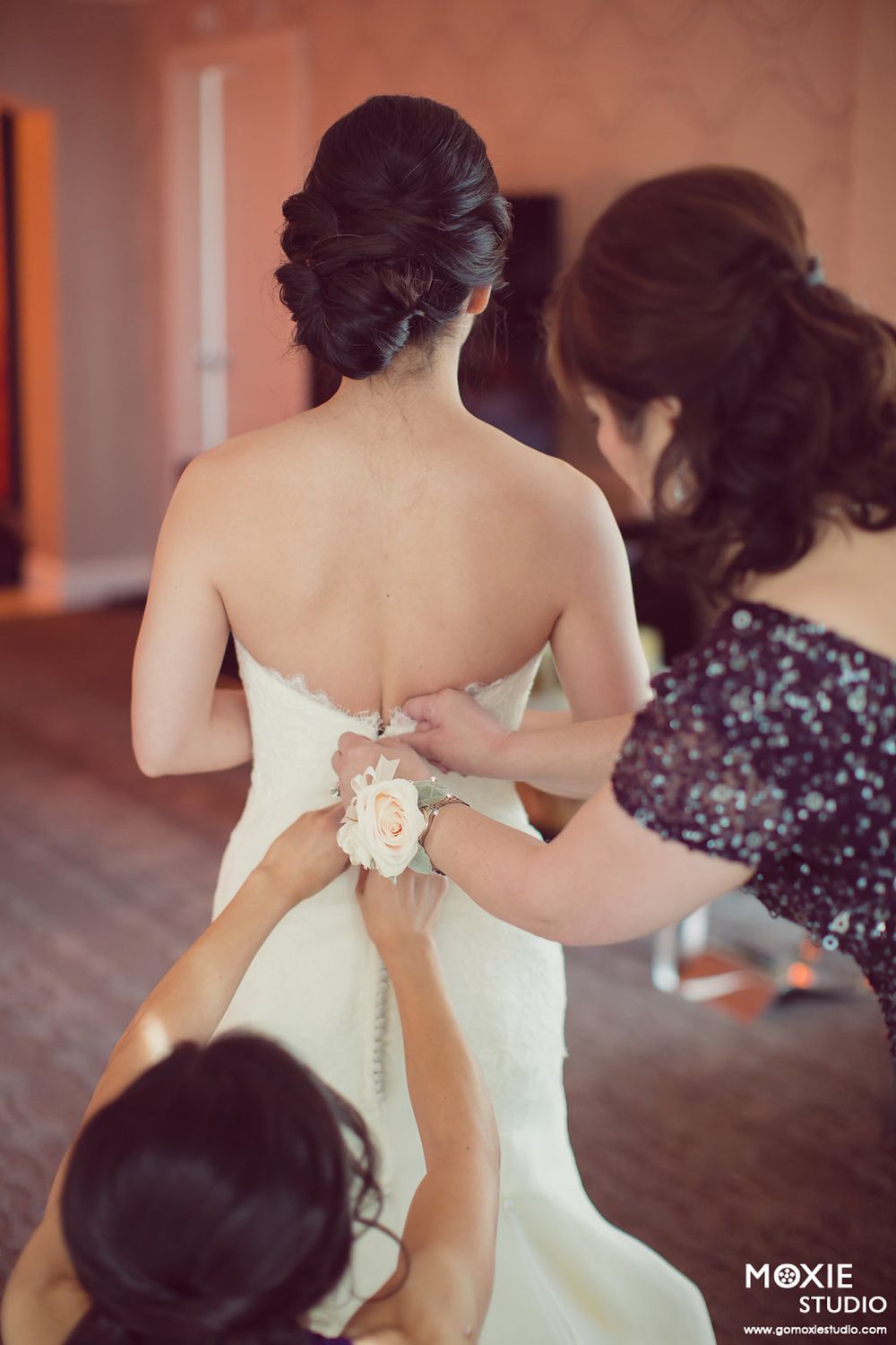 Bridesmaids help button up the back of an elegant white strapless wedding gown during wedding preparations.