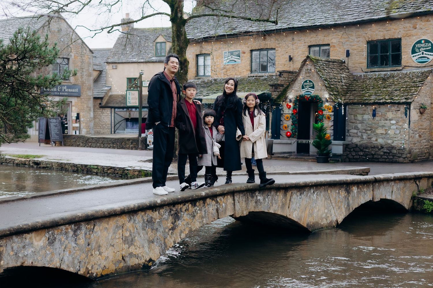 People walking along a stone footbridge over a stream in the picturesque Cotswolds village of Bourton-on-the-Water.