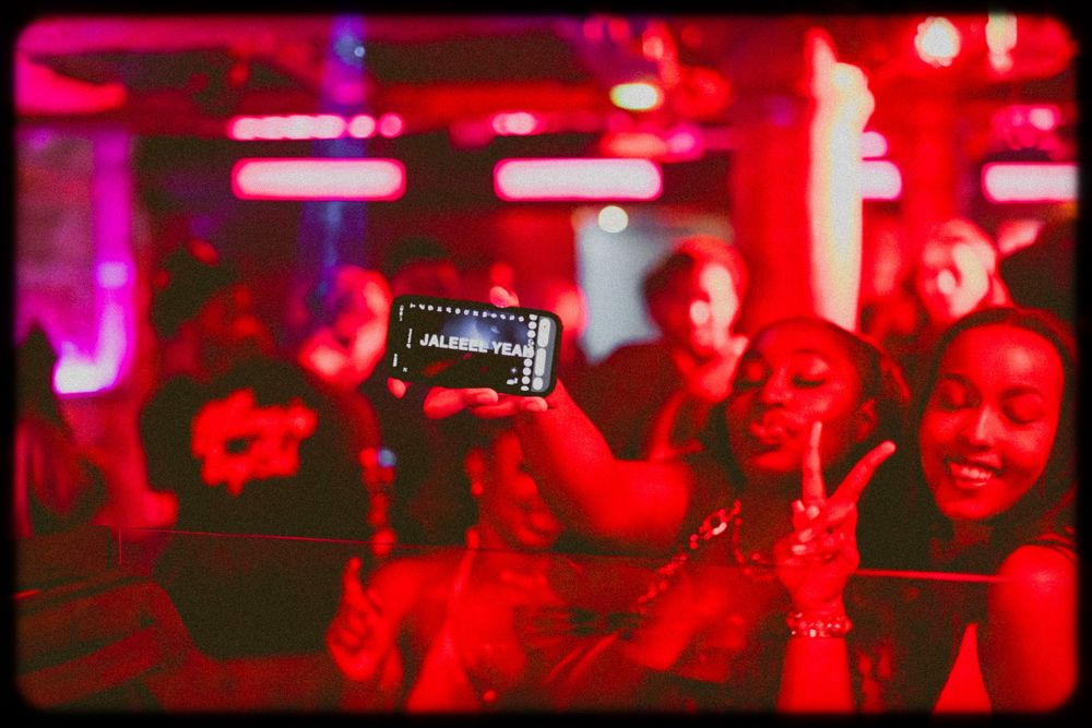 Concert crowd bathed in red lighting holds up phone to record performance at nightclub.