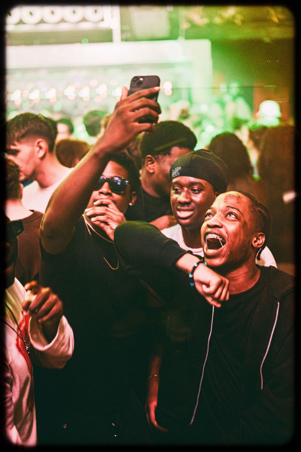 Crowd of partygoers enjoying themselves at a nightclub with phones raised and excited expressions in vintage film style.