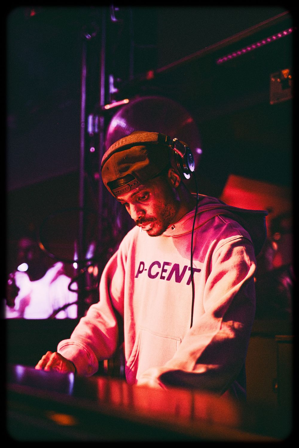 DJ performs at nightclub with red lighting and mixing equipment in dark atmospheric setting.