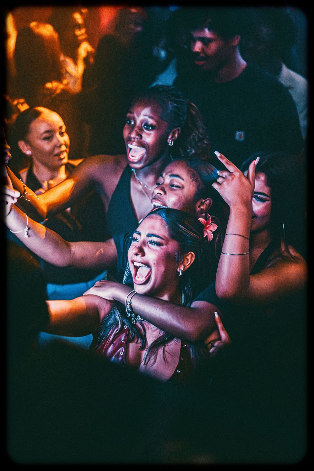 People dance and celebrate at a vibrant nightclub with dramatic orange and blue lighting creating an energetic atmosphere.