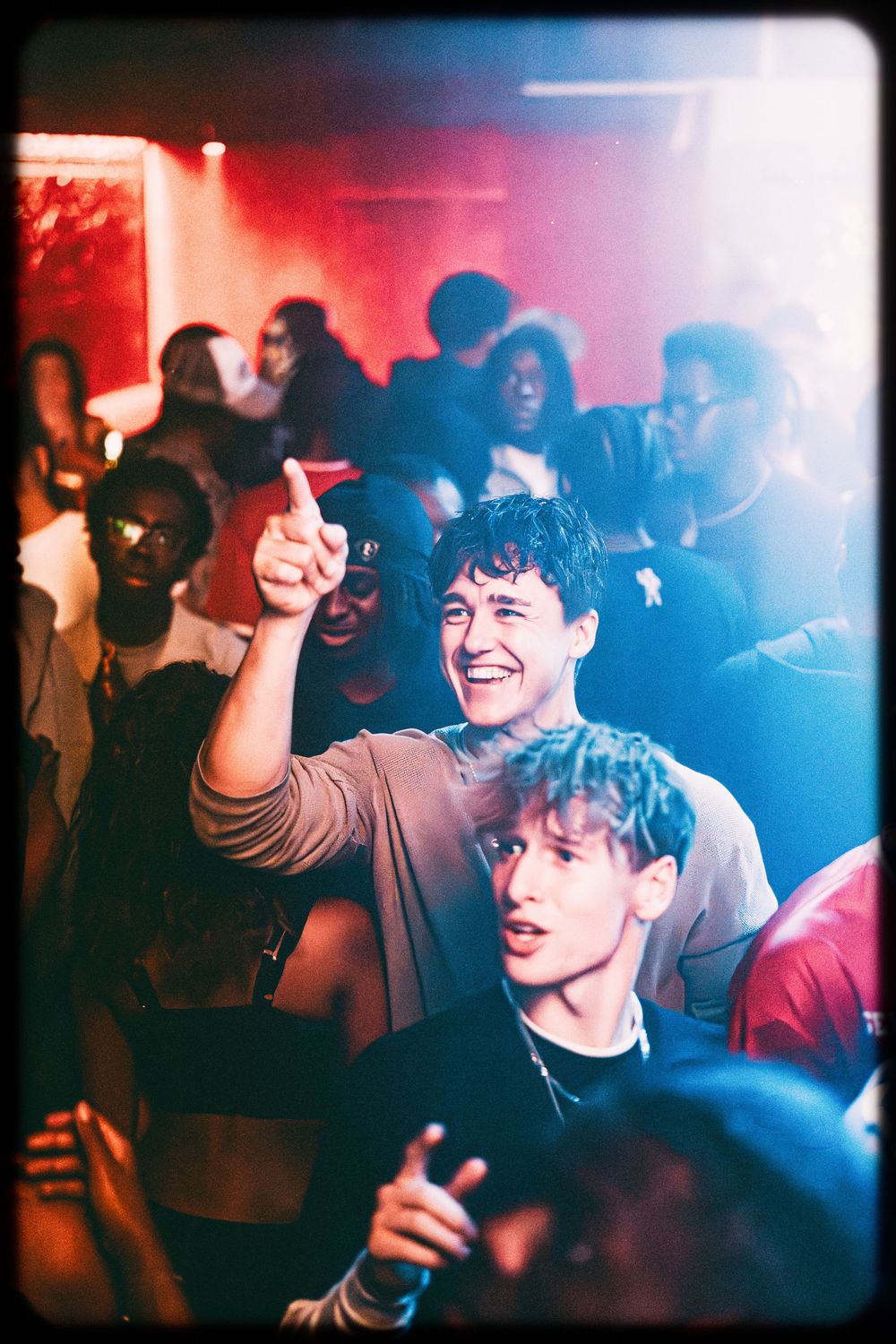 People dancing and celebrating in a nightclub with red and blue lighting creating an energetic party atmosphere.