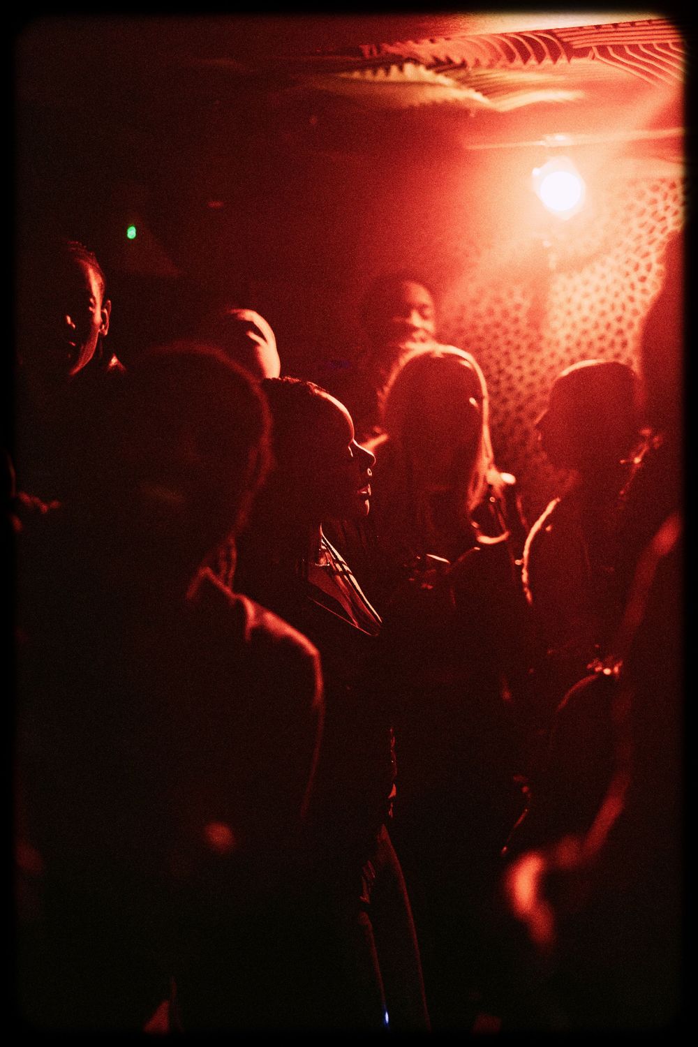 Silhouettes of people dancing in a nightclub under red lighting with disco ball reflections creating a moody atmosphere.
