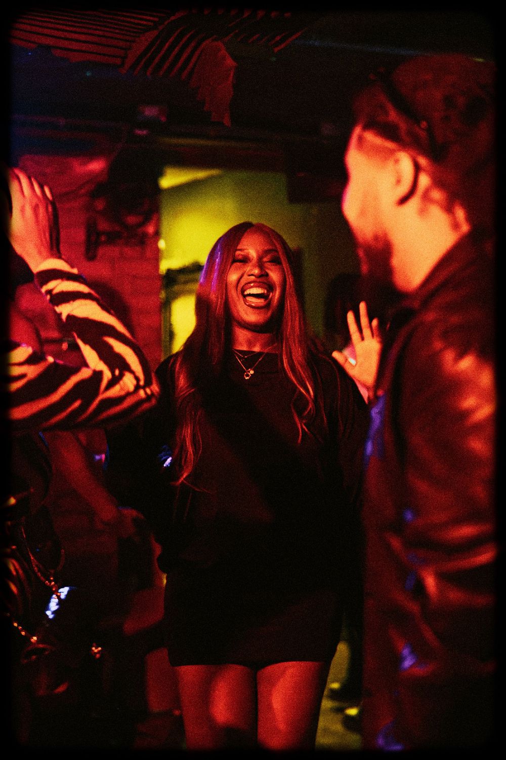 People dancing and socializing in a dimly lit nightclub with red and yellow lighting creating an energetic atmosphere.
