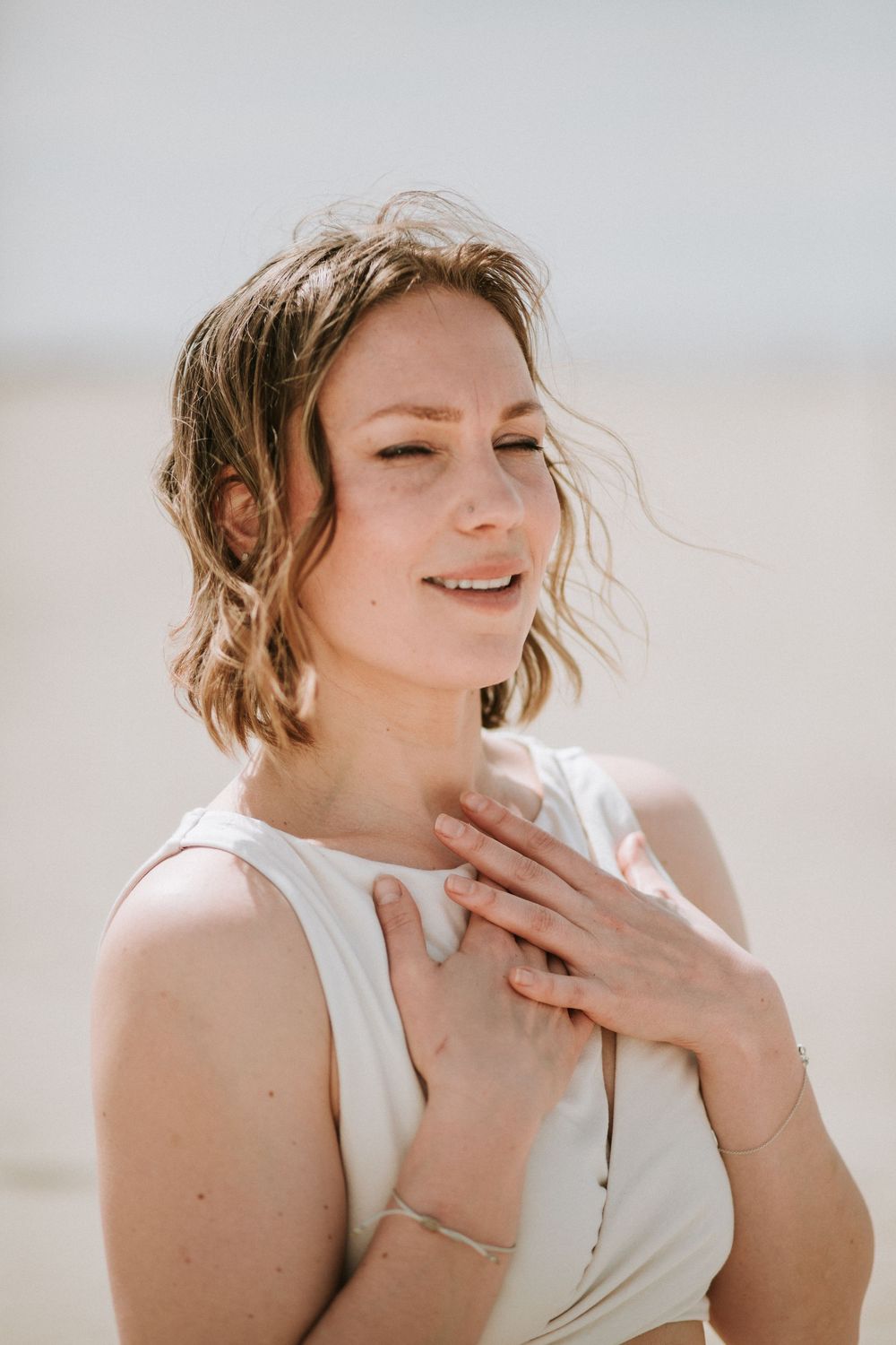 Close-up portrait of a smiling woman in a white top on a bright beach setting.
