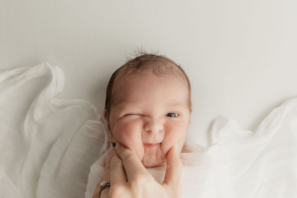 Newborn photo featuring mama's hand squeezing baby's chubby cheeks, taken by Jen Knightstep, Photographer