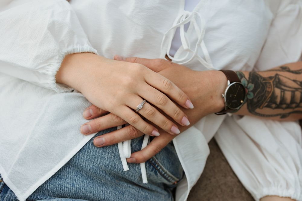 Close-up view of hands holding engagement ring during romantic proposal on white bedding.