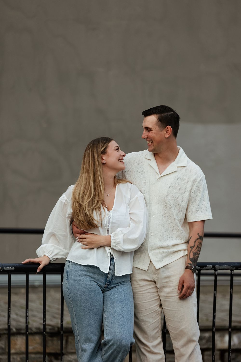 A couple in casual white outfits shares candid moments while leaning against a railing in a series of connected photos.