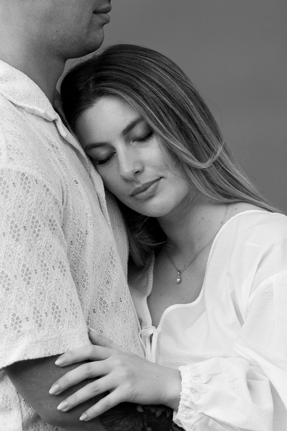 Intimate black and white portrait of a couple embracing, with her head resting gently against his chest.