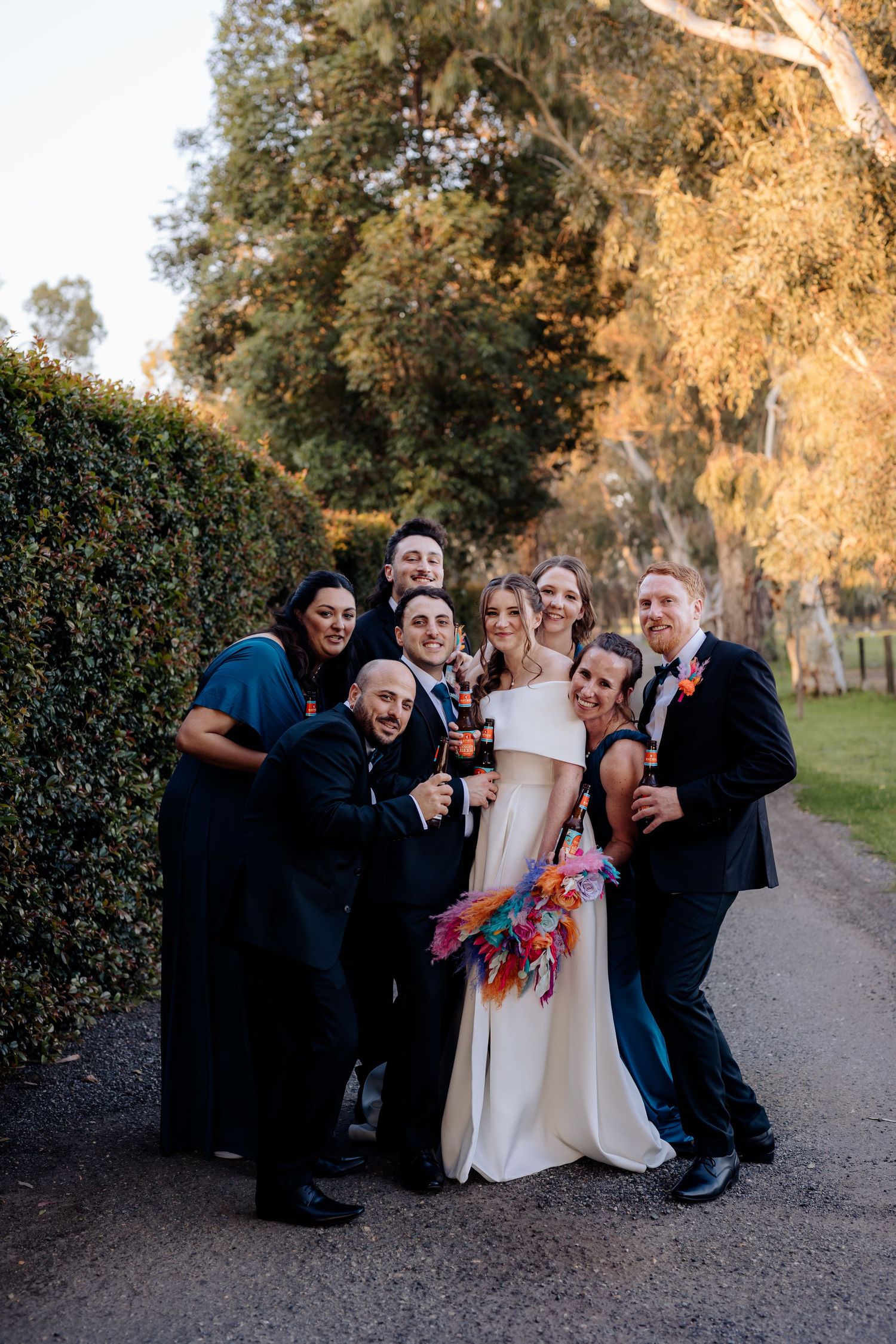 Wedding party poses together on a tree-lined path during golden hour sunset lighting.