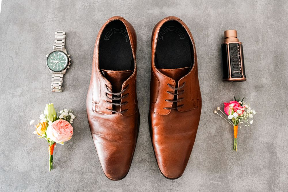 Brown leather dress shoes paired with delicate floral boutonnieres on a gray textured surface.