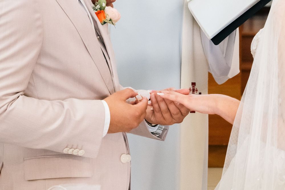 Two people in white formal attire shake hands in a bright indoor setting during a ceremony.