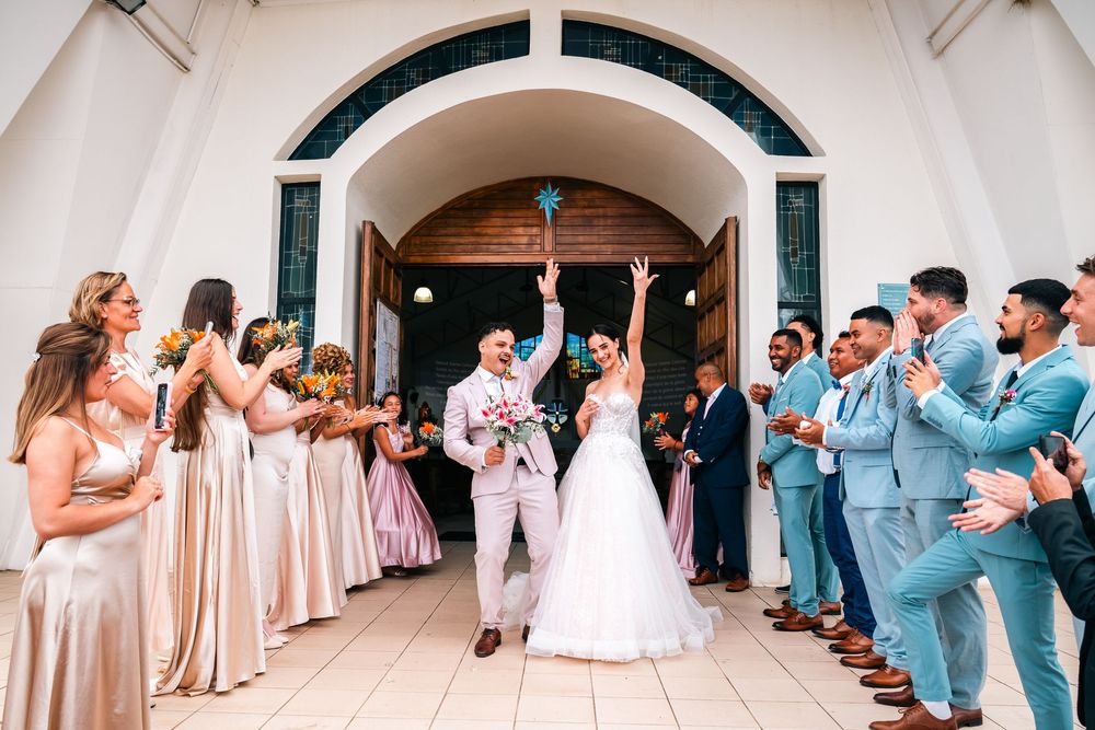 Wedding party celebrates outside church entrance with bridesmaids in blush gowns and groomsmen in light blue suits.