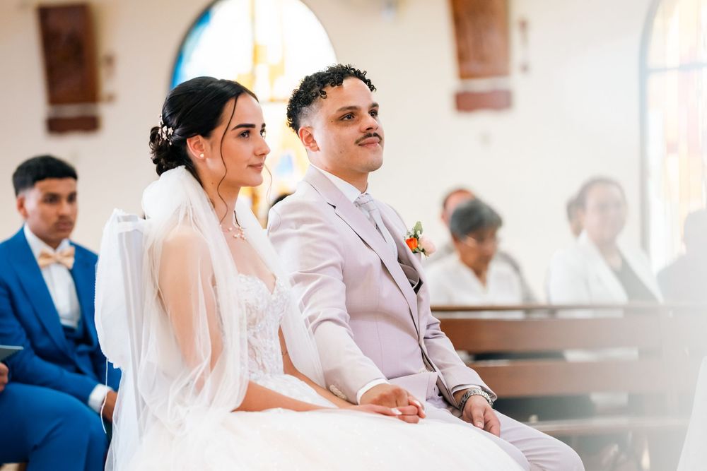 Wedding guests seated at long tables in a bright reception hall share laughter and conversation during a celebration.