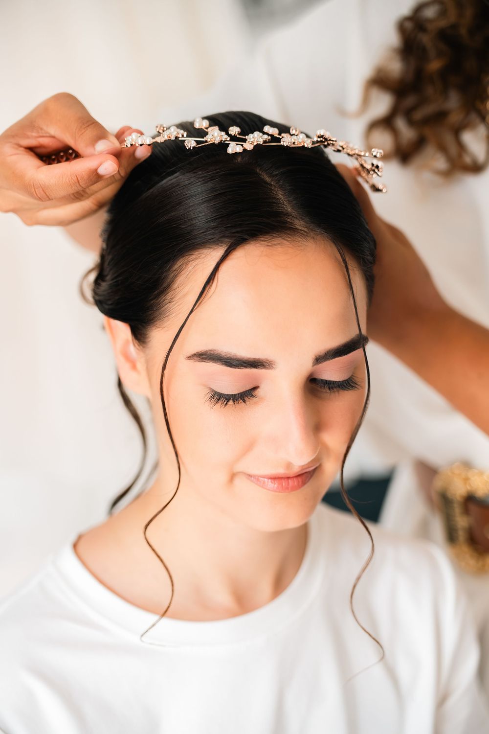 A delicate bridal hair accessory being placed on dark hair during wedding preparations.