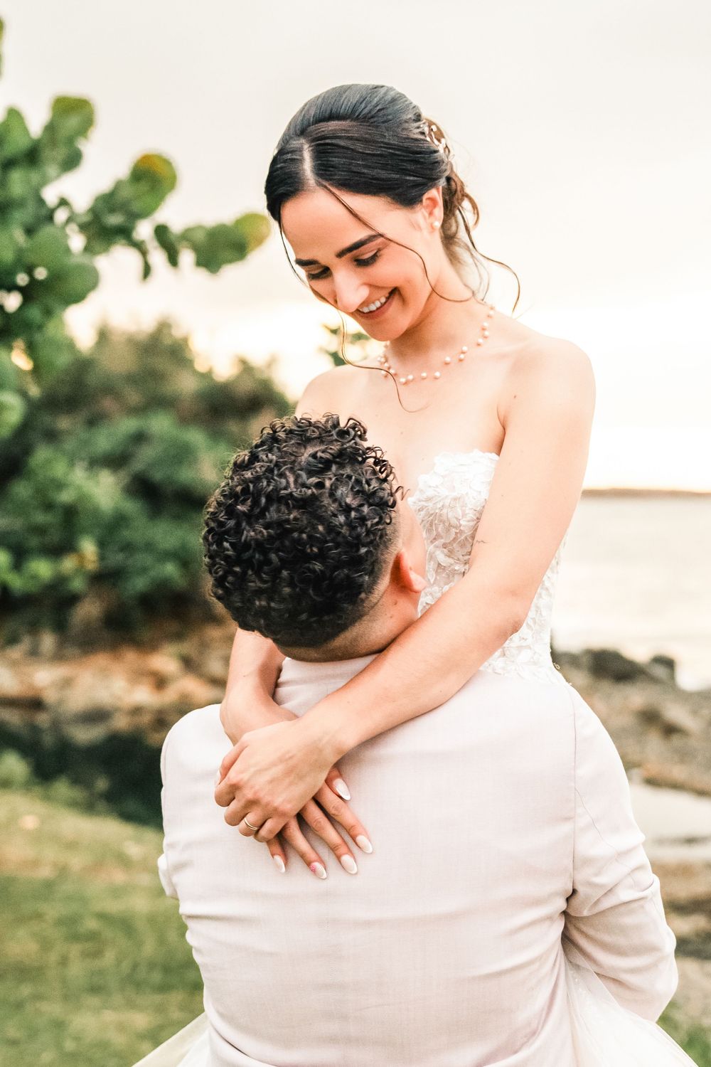 A romantic wedding moment captured outdoors with a couple embracing against a natural backdrop at sunset.