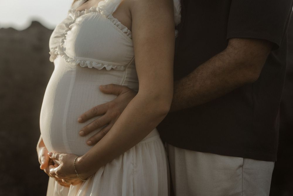 A series of maternity photos showing a pregnant belly in a white dress against a dark background.