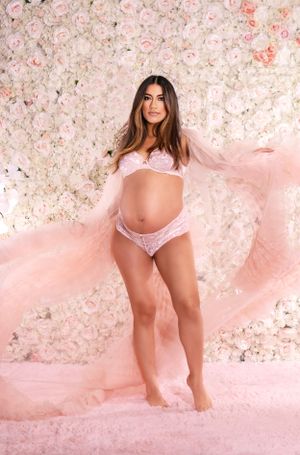 Romantic boudoir photography with flowing pink fabric and floral wall backdrop.