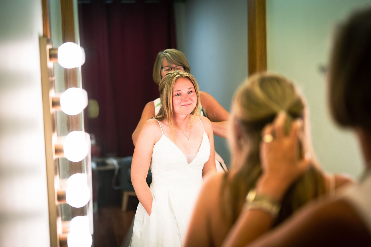 Woman in white dress getting ready in front of illuminated mirror in dressing room.