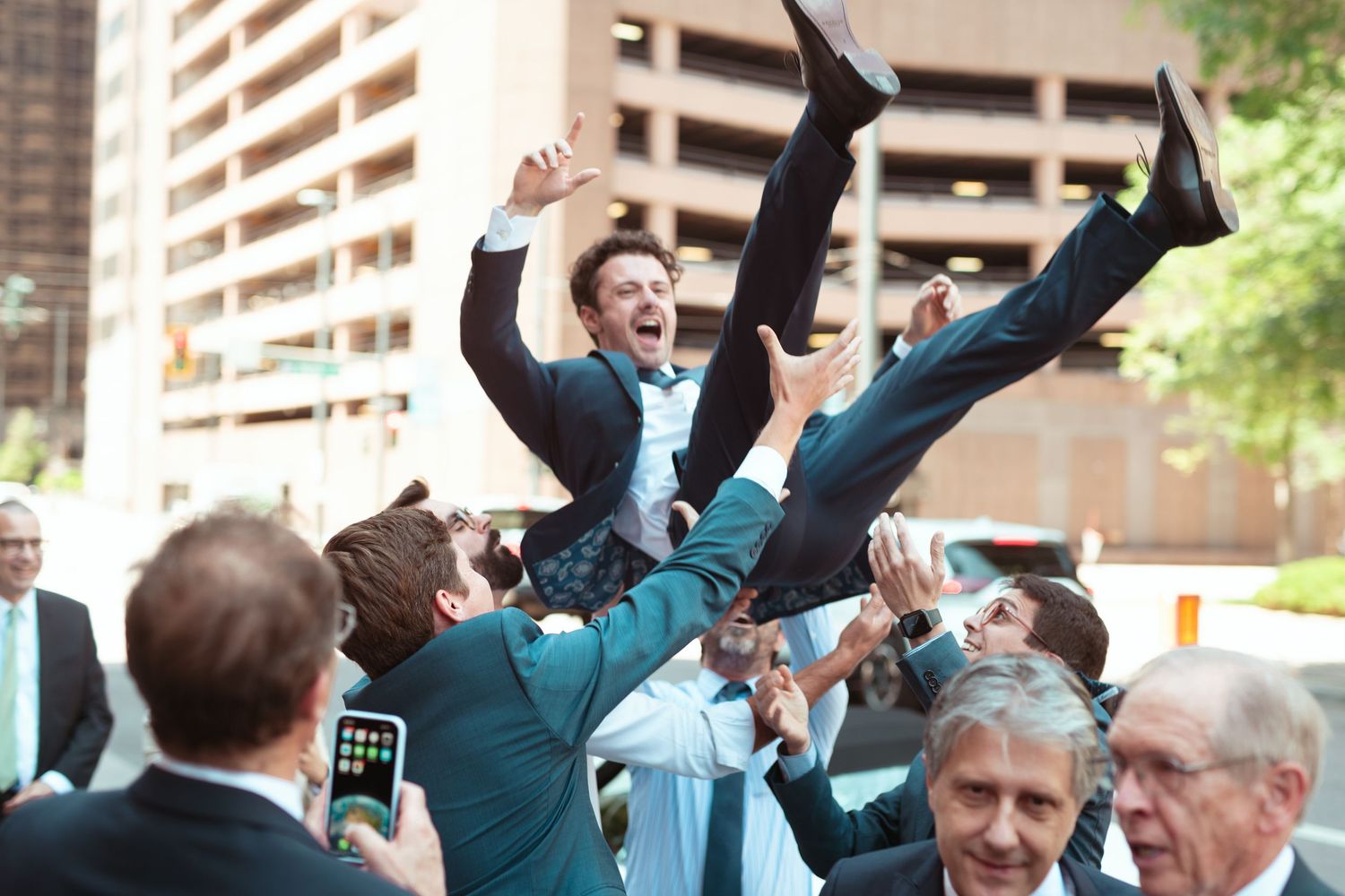 Groomsmen in teal suits celebrating and cheering outdoors near apartment buildings.