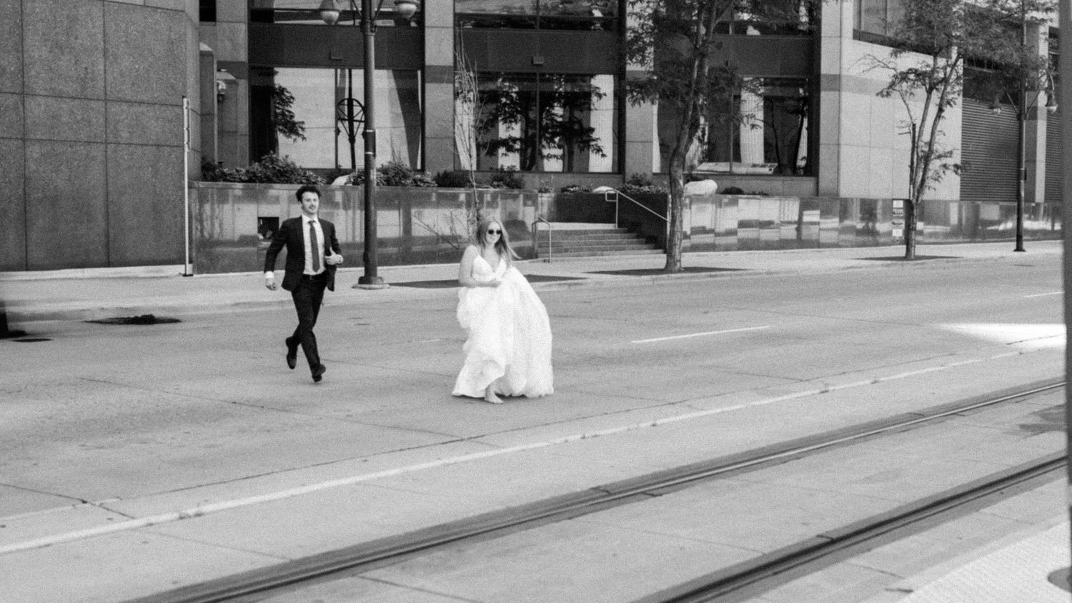 Wide urban street view with pedestrians walking past modern buildings in black and white photography.