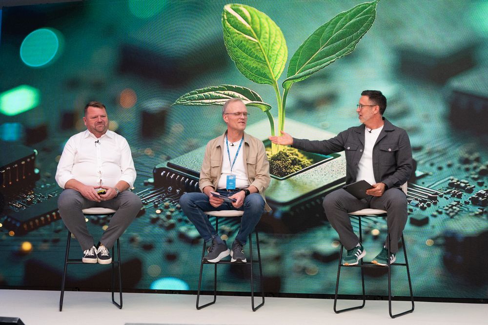 Three panelists seated on stage with a green plant graphic projected on the screen behind them.