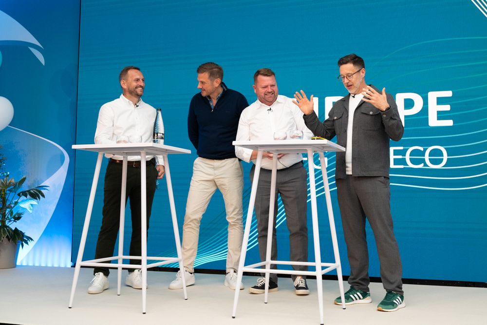Group of people sitting on white bar stools against a bright blue backdrop at an event.
