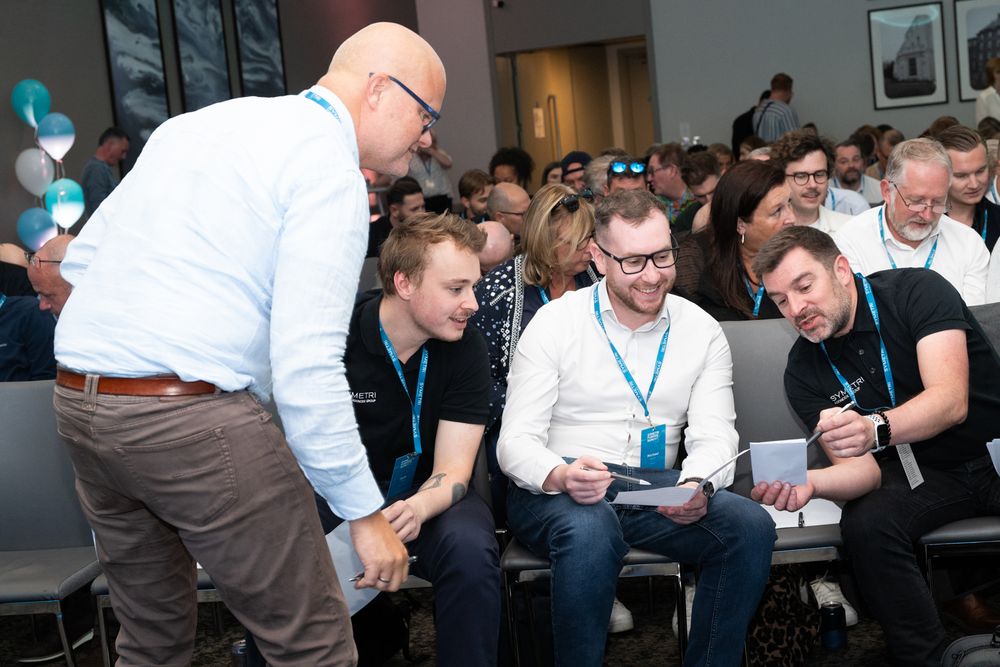 A group of people sit at tables working together during a collaborative workshop or meeting session.
