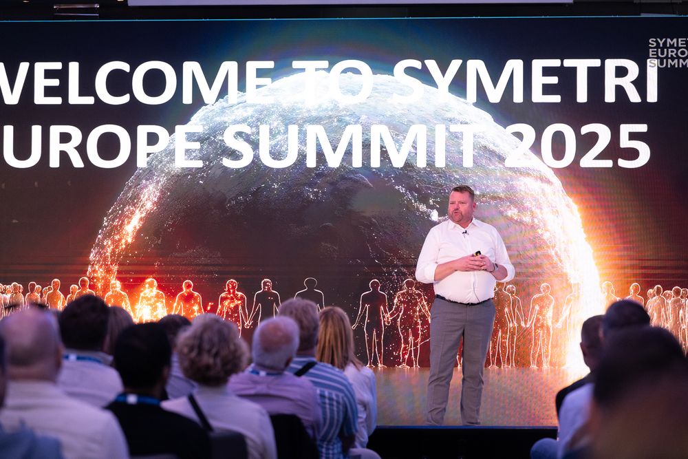 A presentation at a corporate summit with a large illuminated display screen showing event branding.