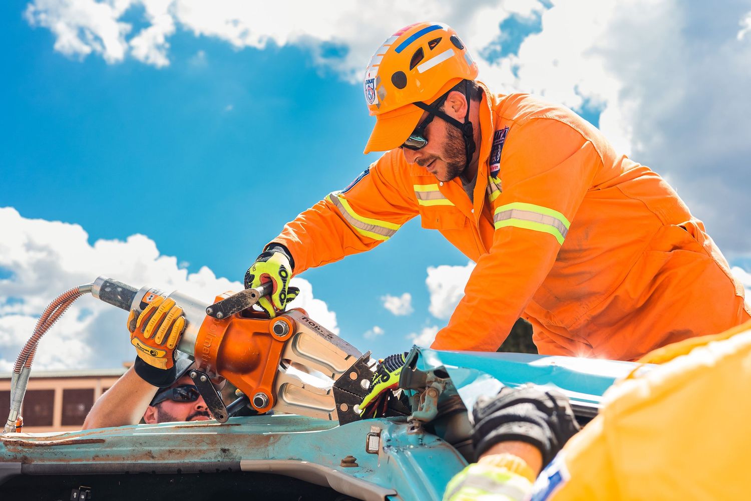 Worker in orange safety gear performs maintenance on solar panels against bright blue sky with white clouds.