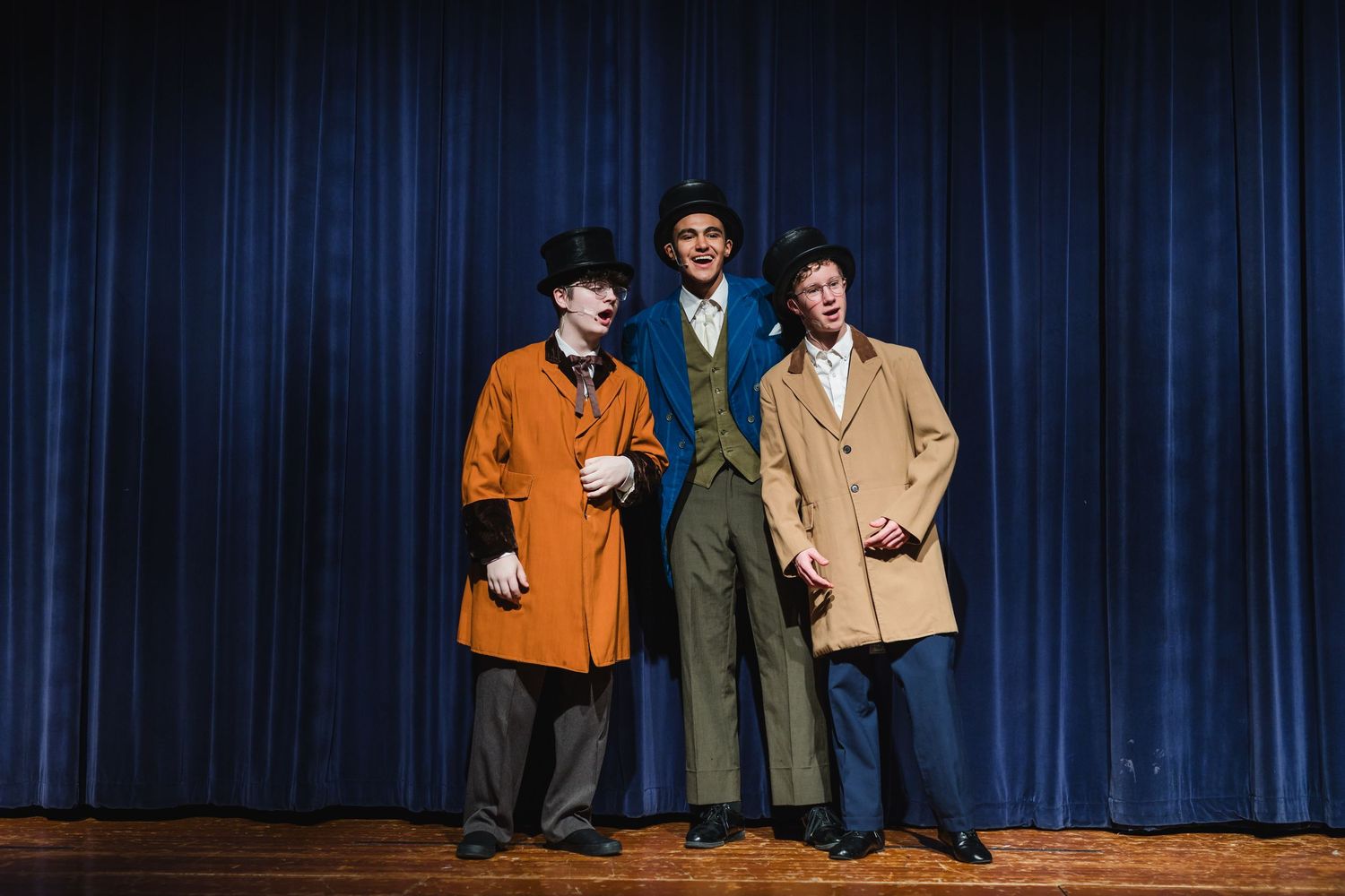Group performs on stage in front of dark blue curtain backdrop during theater production.