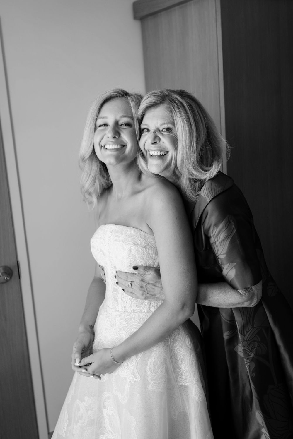 A candid black and white photo showing joyful laughter between two women, one wearing a white wedding dress.