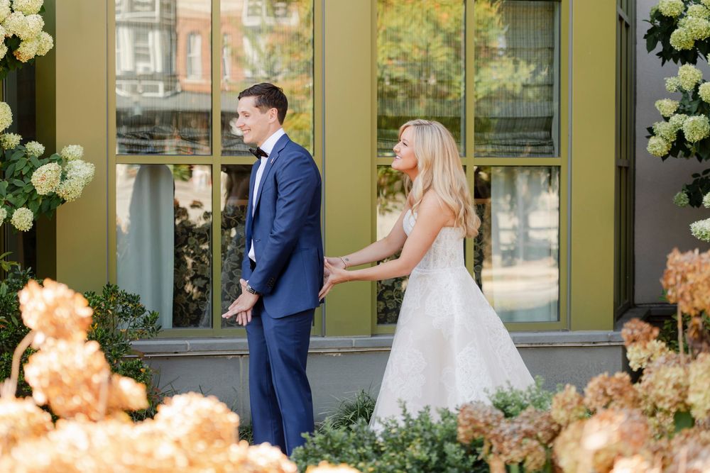 A couple in wedding attire stands together in front of a building decorated with elegant white floral arrangements.