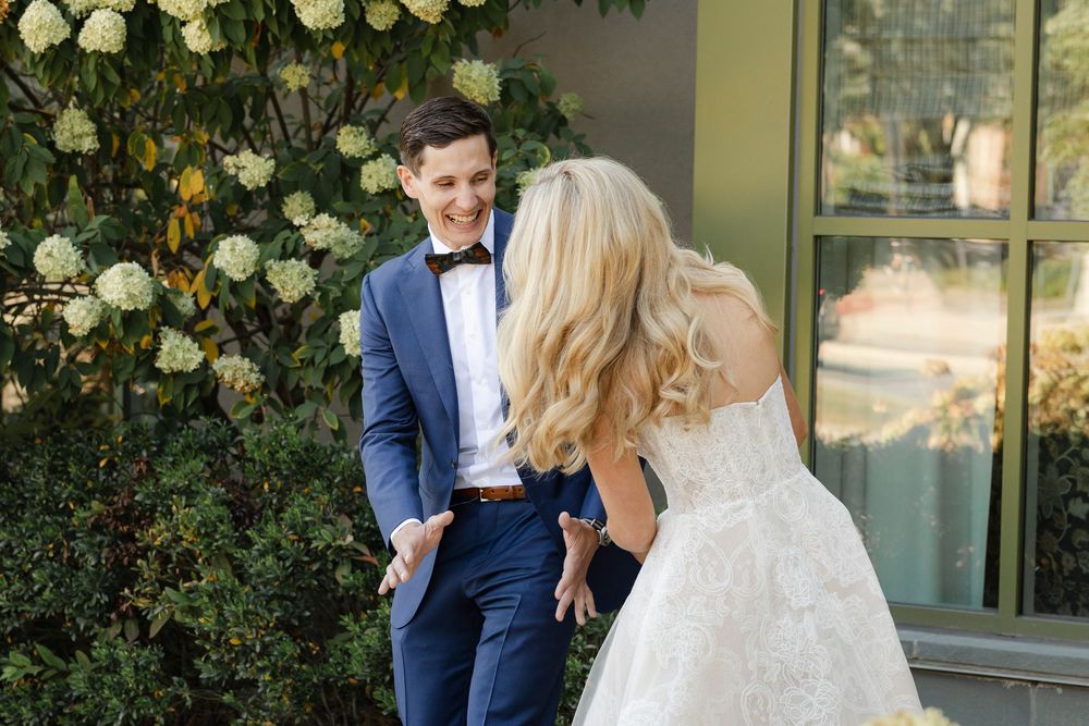 A bride and groom share a romantic moment in a garden setting with white roses and greenery.