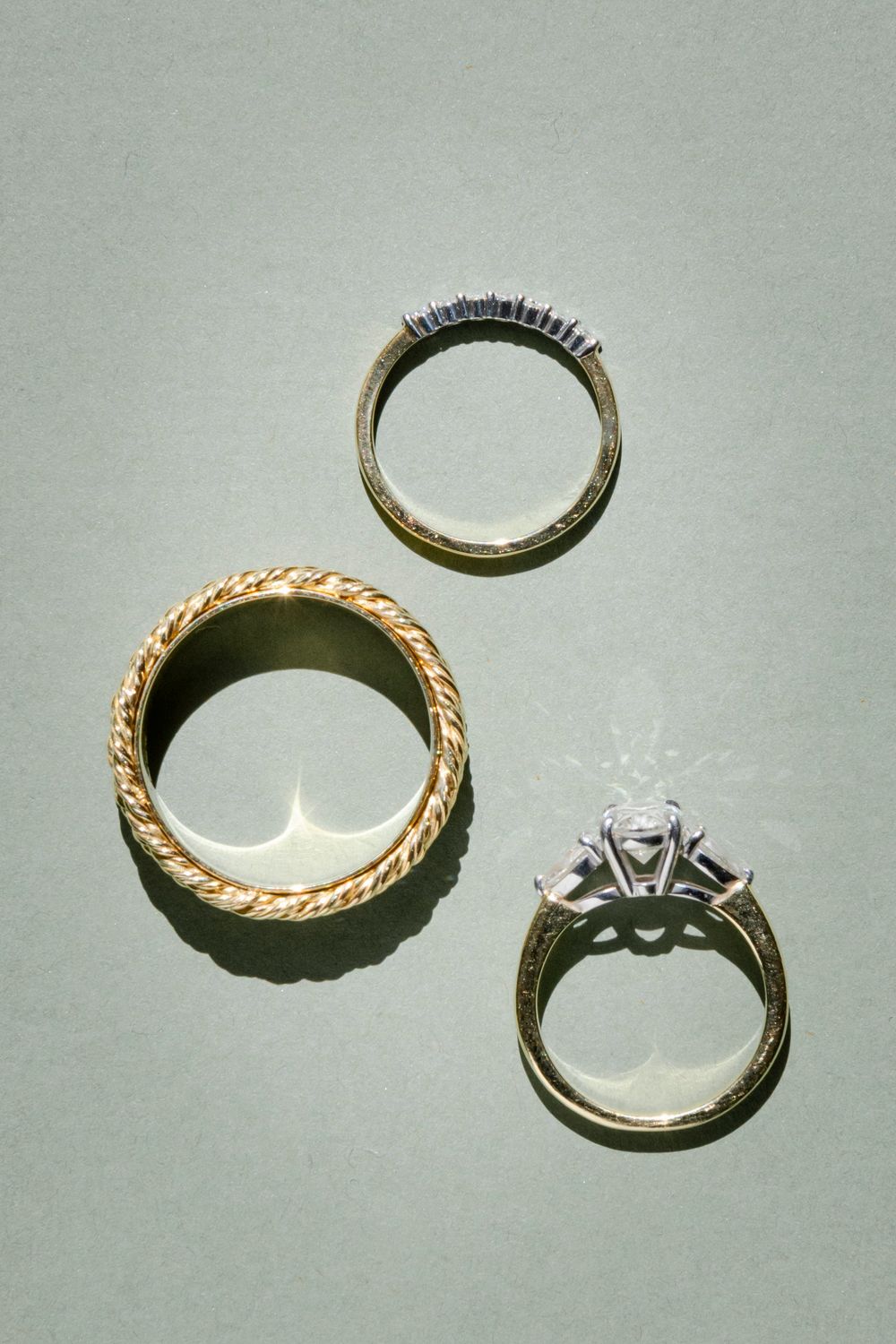 Close-up view of three gold engagement rings with different band styles and diamond settings against a light gray background.