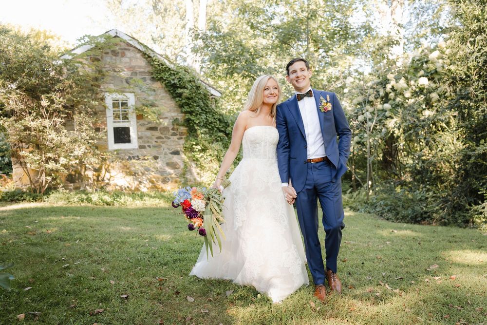 A wedding couple walks hand in hand through a sunlit garden path on their special day.
