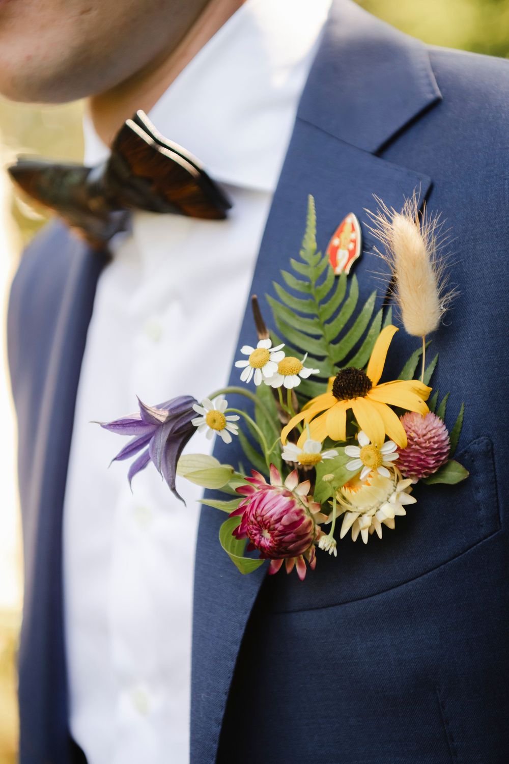 Colorful floral boutonnieres with sunflowers, wildflowers and greenery pinned to navy blue suit jackets.