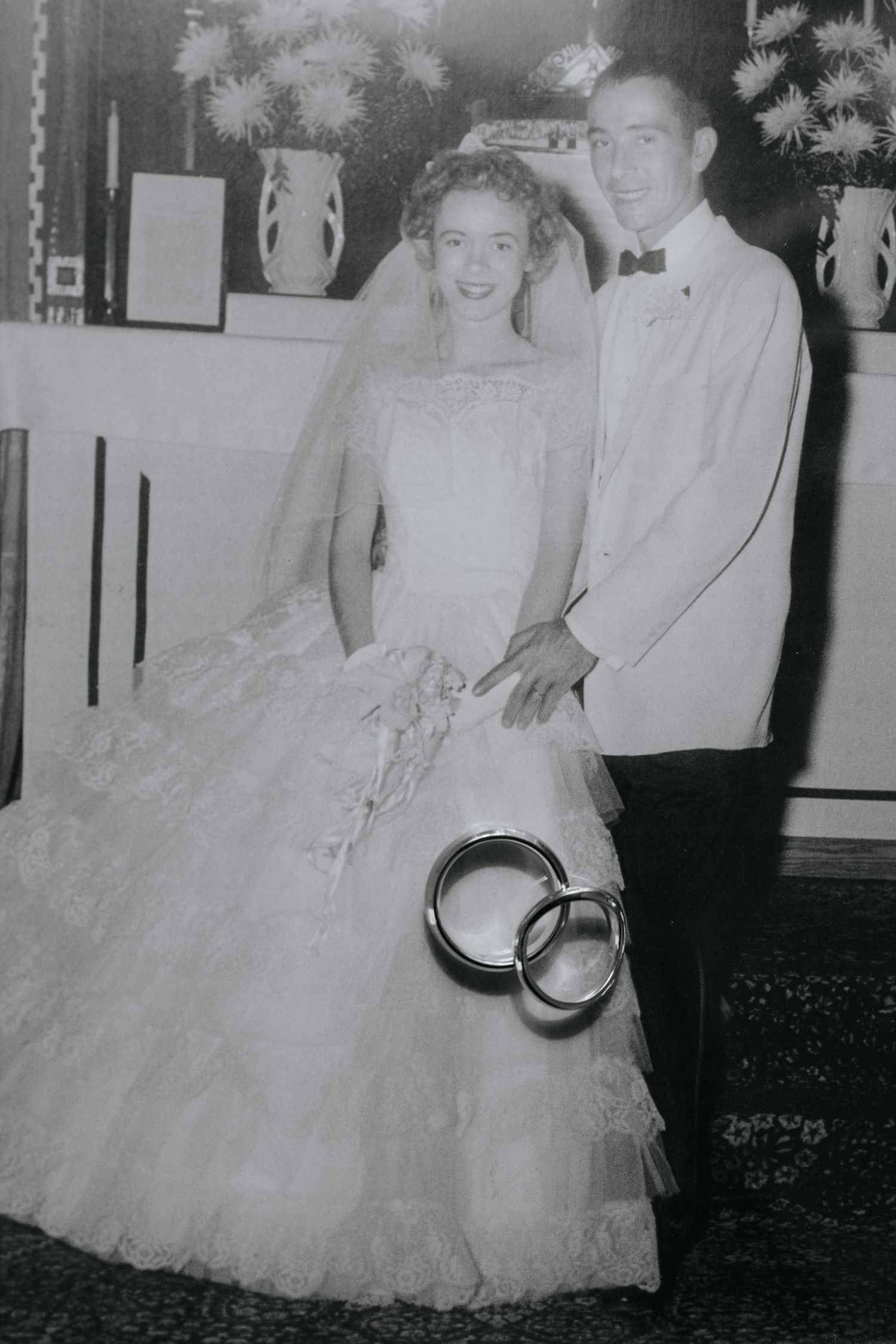 Black and white vintage wedding photograph with wedding rings displayed in foreground.