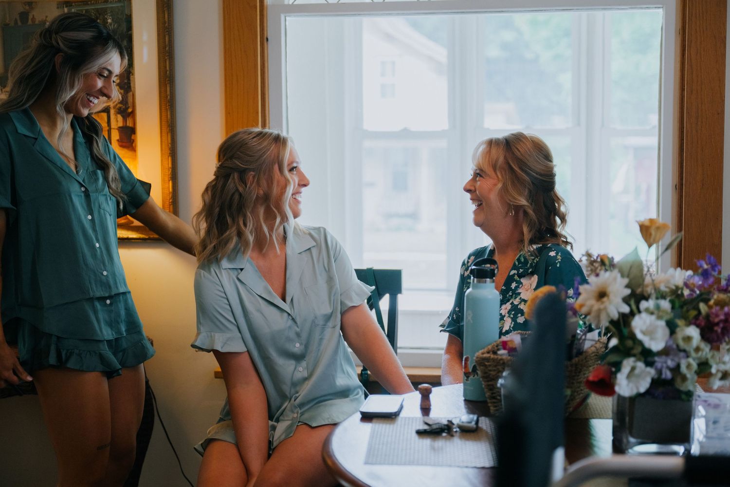 Wedding party gathered by a window with natural light and floral decorations.