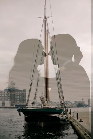 Silhouetted figures against a harbor backdrop with sailboats and city buildings in the background.