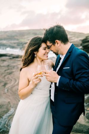 A couple shares an intimate moment while holding champagne glasses against a scenic mountainous backdrop at sunset.