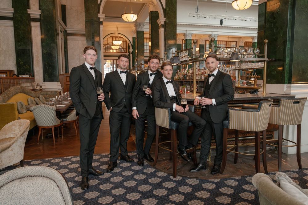 A group in formal attire gathers in an elegant restaurant with warm lighting and classic architectural details.