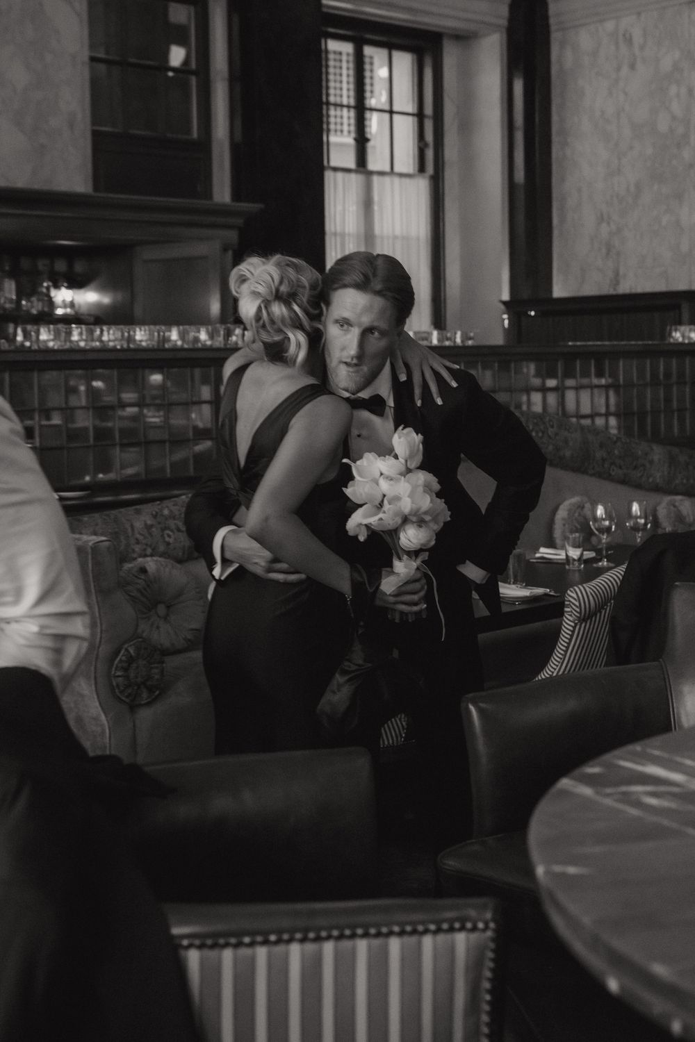 Intimate black and white photo of newlyweds embracing on a vintage leather couch.