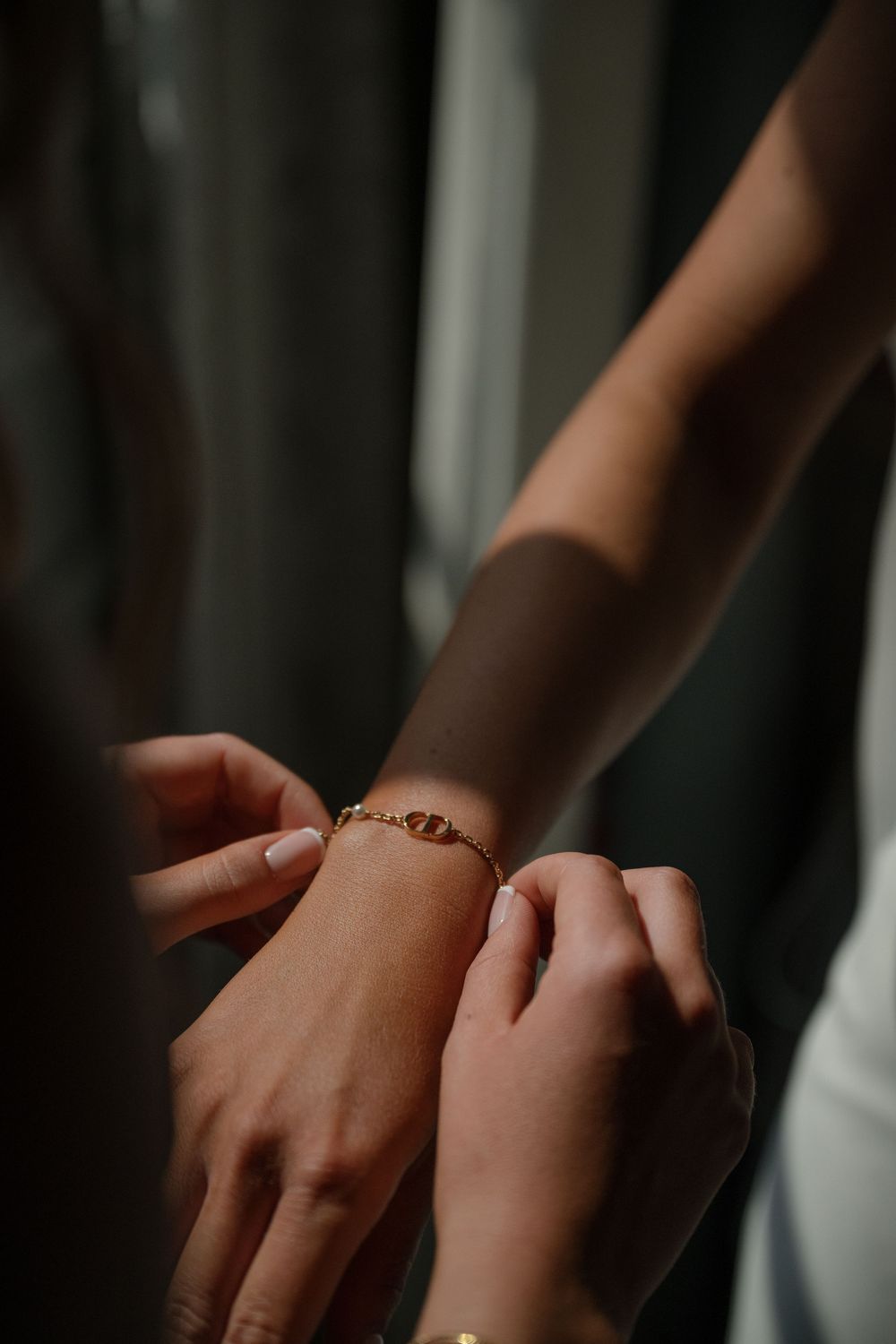 Close-up shot of hands fastening a delicate bracelet around a wrist in moody lighting.