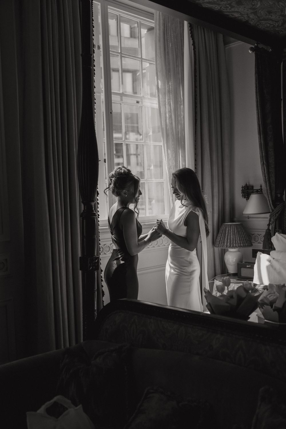 Two silhouettes stand together by a window in an elegant room, creating a romantic black and white moment.
